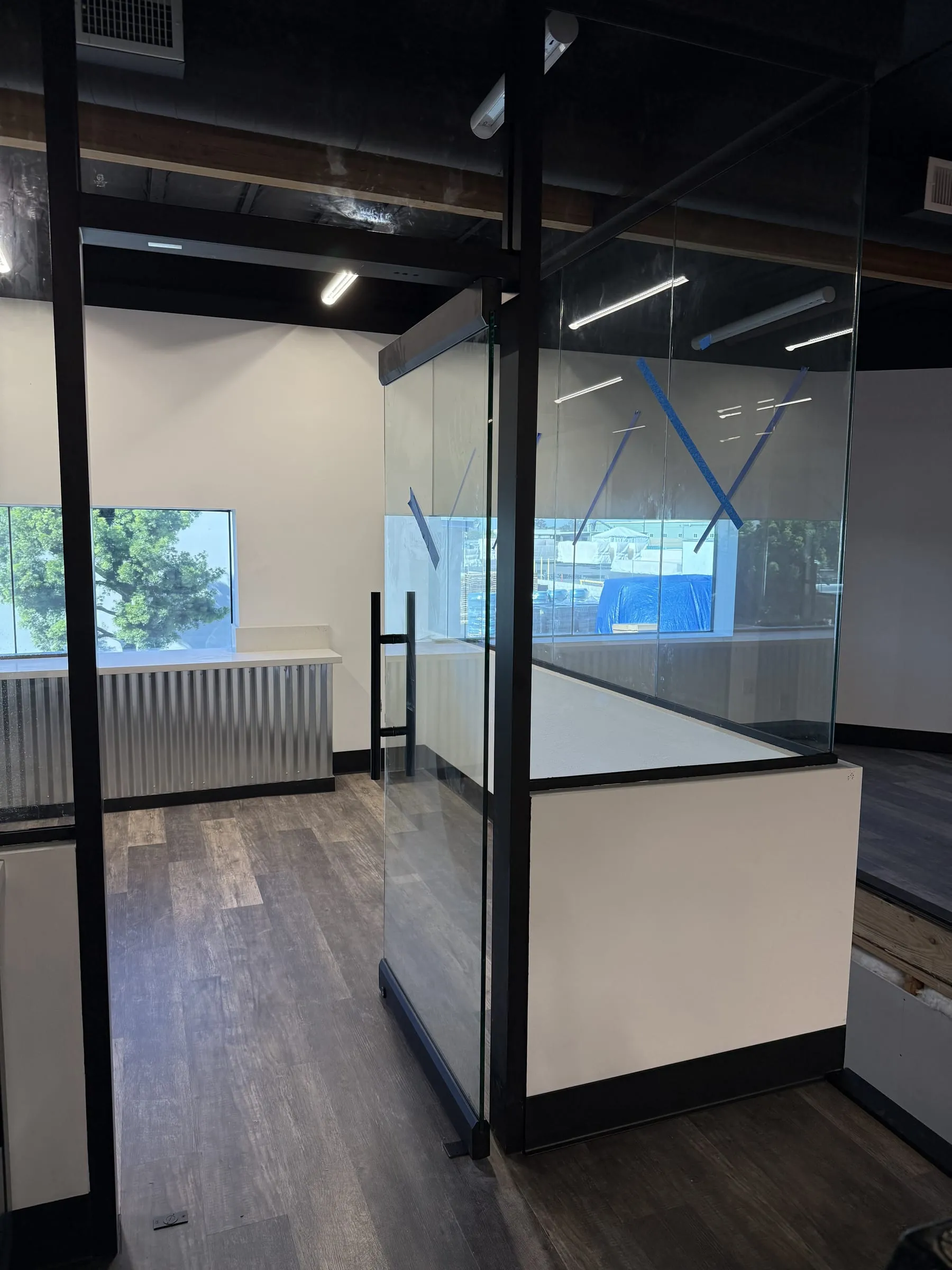 Black-framed glass office partitions with a glass door above a white half wall