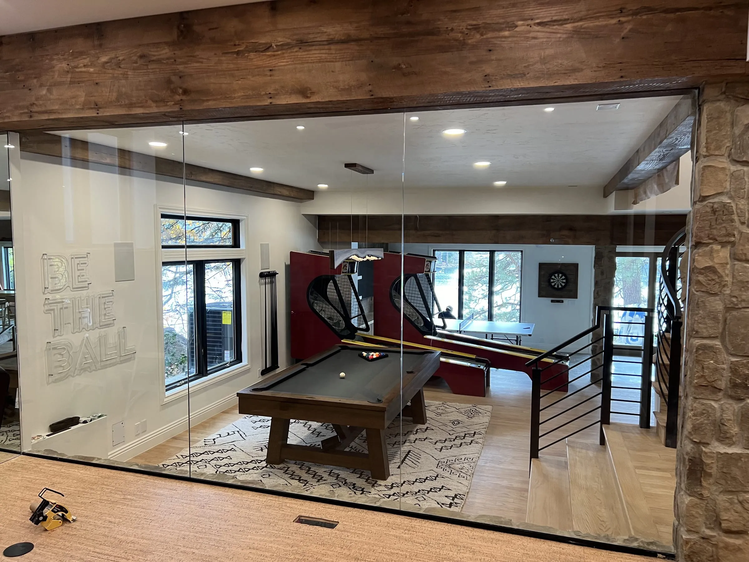 Frameless glass partition under a timber beam, looking into a billiards room