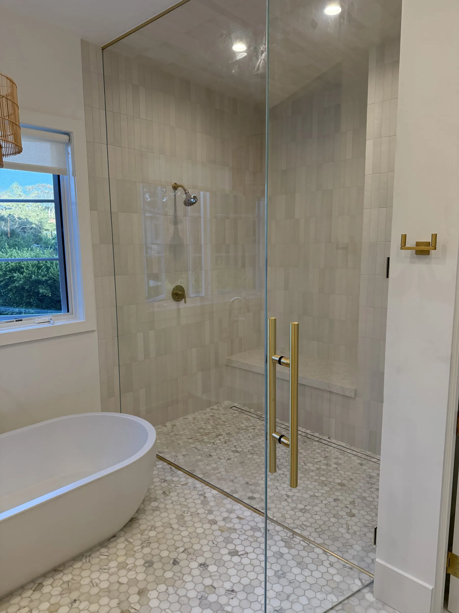 Frameless glass shower door and fixed panel with brass hinges and a ladder pull