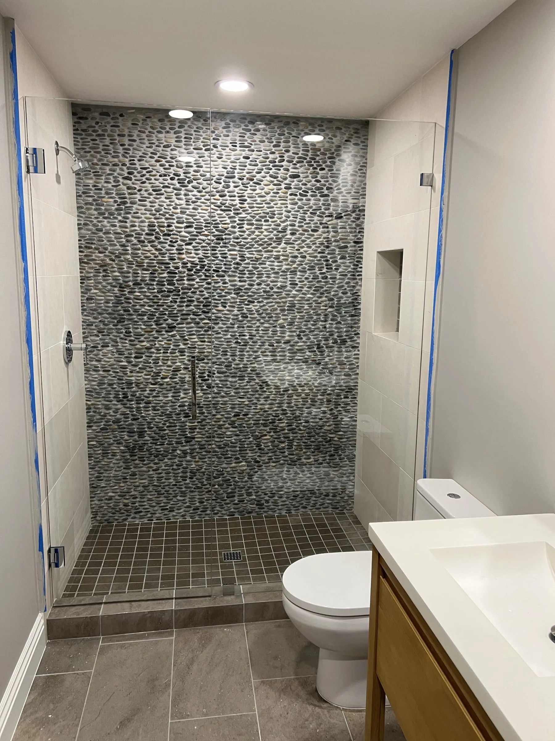 Frameless glass shower door and panel against a river-pebble wall