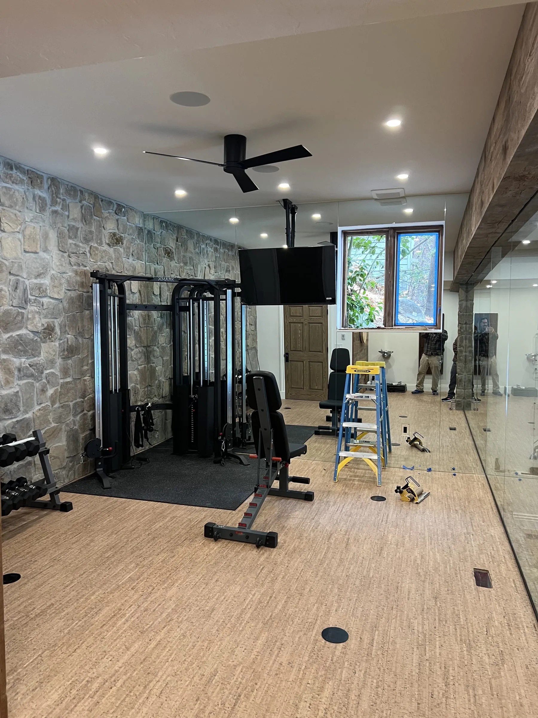 Home gym with wall mirrors around the window, a ladder and tools still on the floor