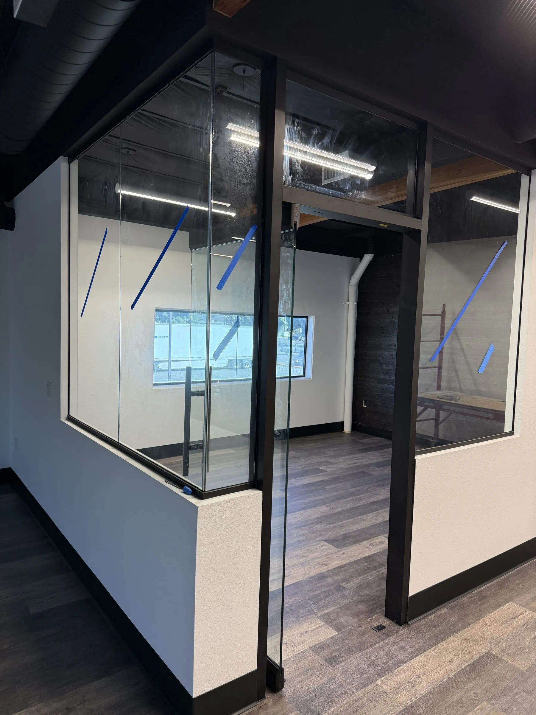 Corner of a glass office enclosure with black frames above a half wall
