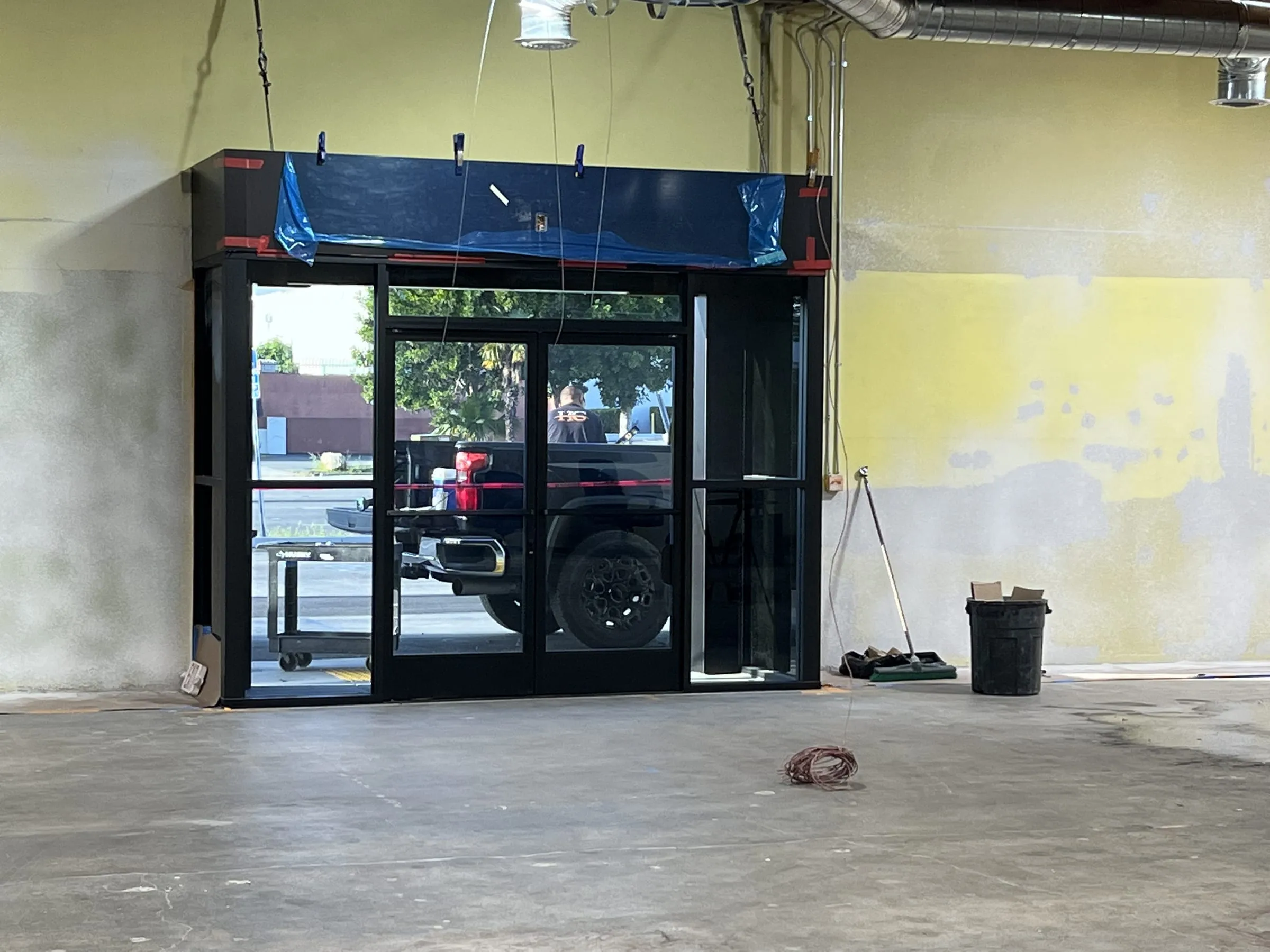 Black storefront entrance with glass doors installed in an unfinished interior, protective film on the header